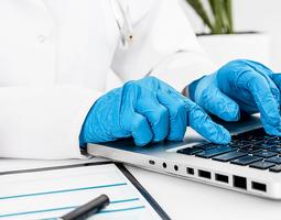 A doctor in gloves working on laptop